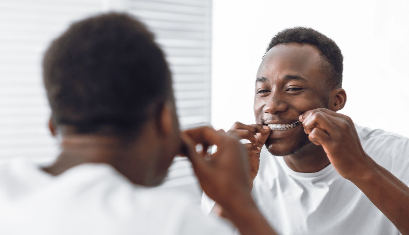 man flossing his teeth through mirror