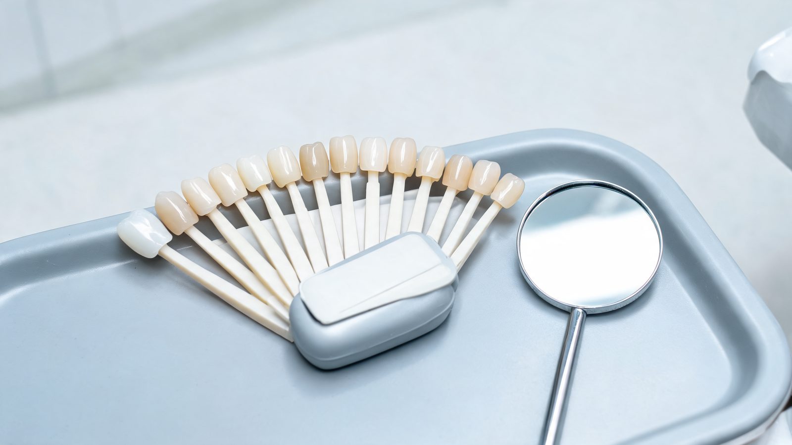 Porcelain shade guide with tooth colored tabs in slightly different shades beside a hand mirror